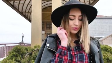 Limanda, yatların yanında poz veren kız, kısa bir elbise, yuvarlak bir şapka ve yüksek çizmelerle yürüyor, gülümsüyor.