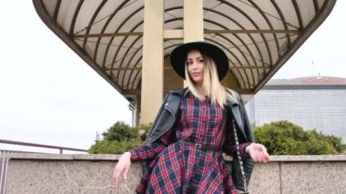 Limanda, yatların yanında poz veren kız, kısa bir elbise, yuvarlak bir şapka ve yüksek çizmelerle yürüyor, gülümsüyor.