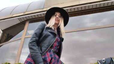 Limanda, yatların yanında poz veren kız, kısa bir elbise, yuvarlak bir şapka ve yüksek çizmelerle yürüyor, gülümsüyor.