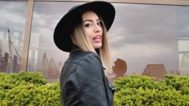 Limanda, yatların yanında poz veren kız, kısa bir elbise, yuvarlak bir şapka ve yüksek çizmelerle yürüyor, gülümsüyor.