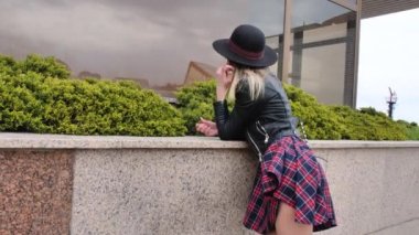 Limanda, yatların yanında poz veren kız, kısa bir elbise, yuvarlak bir şapka ve yüksek çizmelerle yürüyor, gülümsüyor.