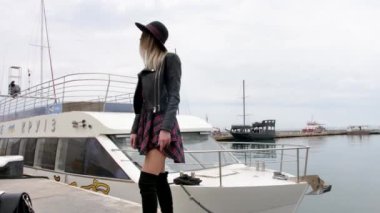 Metal bir kabloya yakın poz veren, efsanevi beyaz ayakkabılar giyen, kot ceket giyen, dans eden, gülümseyen bir kız.
