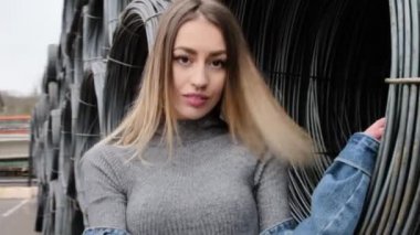 Metal bir kabloya yakın poz veren, efsanevi beyaz ayakkabılar giyen, kot ceket giyen, dans eden, gülümseyen bir kız.