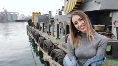 Metal bir kabloya yakın poz veren, efsanevi beyaz ayakkabılar giyen, kot ceket giyen, dans eden, gülümseyen bir kız.