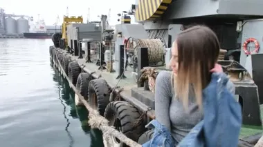 Metal bir kabloya yakın poz veren, efsanevi beyaz ayakkabılar giyen, kot ceket giyen, dans eden, gülümseyen bir kız.