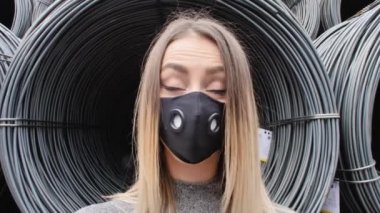 Limanda metal bir kabloya yakın poz veren, efsanevi beyaz ayakkabılar giyen, kot ceket giyen, dans eden, gülümseyen, yüzüne maske takan bir kız.