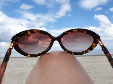 Çıplak ayaklar, plajda renkli güneş gözlükleriyle yükseldi. Arka planda güzel deniz sörfü ve mavi güneşli gökyüzü. Yaz tatili