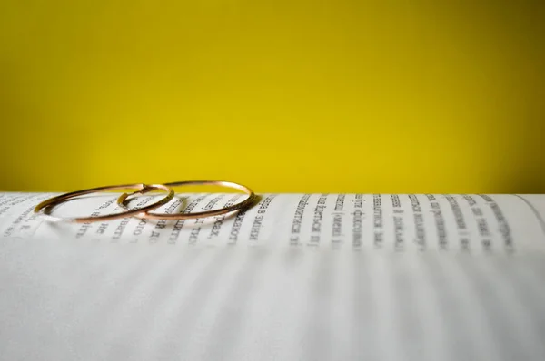 Two gold rings lie on a book among yellow background