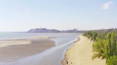 Yazın sanayi şehri. Ufukta deniz kenarında metalürjik bir bitki var.