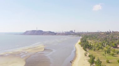 Yazın sanayi şehri. Ufukta deniz kenarında metalürjik bir bitki var.