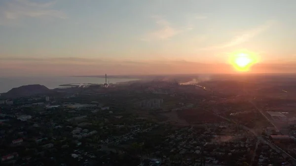 Yazın sanayi şehri. Ufukta deniz kenarında metalürjik bir bitki var.