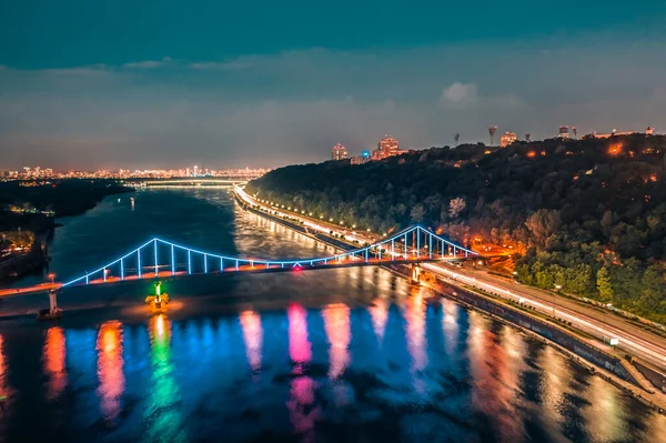 Nachtbild. Bunte Brücke über Fluss und Uferstraße in Kiew Stockbild