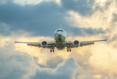Bir jet uçağı öğleden sonra iniş takımlarıyla bulutlu bir gökyüzüne doğru iniyor.