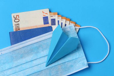 Sağlık maskesi, pasaport ve avroya sahip mavi arka planda bulunan uçak, salgın ya da salgın nedeniyle uçuş yasağı kavramı