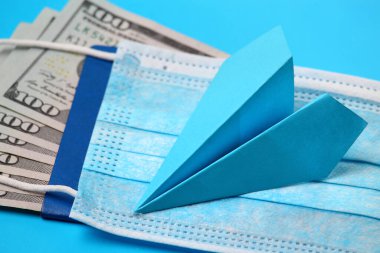 Pasaport, dolar ve tıbbi maskeyle mavi arka planda kağıt uçak, salgın ya da salgın nedeniyle uçuş yasağı kavramı