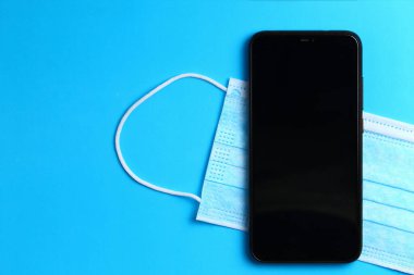 Tıbbi maske ve akıllı telefon mavi arka planda bir yazı veya metin yeri ile