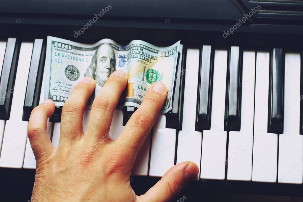 Dollars on piano keys and musician's hand, background, toned