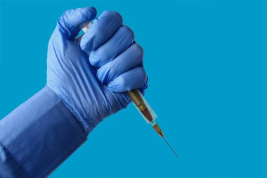 Şırıngada bir kurşun ve tıp eldiveninde bir doktorun eli. Mavi arkaplan