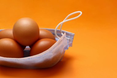 Sarı arka planda tavuk yumurtası ve tıbbi maske. Marketten ya da sepetten bir paket içeren metafor. Koronavirüs salgını sırasında Paskalya konsepti