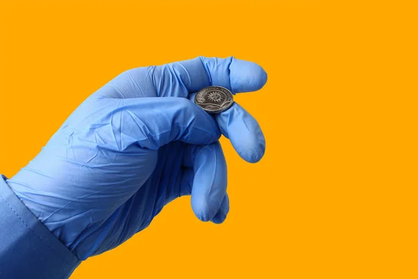 A doctor in a medical glove tosses a coin on an orange background. Symbol of chance
