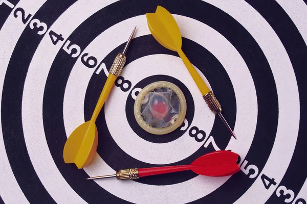 Unpacked condom on the background of a dartboard target (darts), toned. Love triangle concept