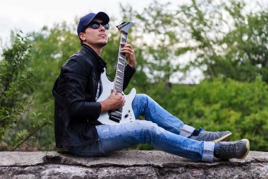 Bulanık arka planda gitarı olan genç bir adam.