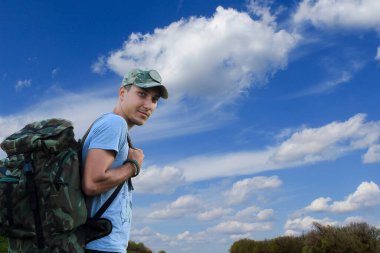 Güzel bulutların arkasında gülümseyen sırt çantalı bir yürüyüşçü.