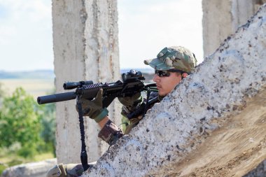 Askeri giysiler içindeki askerler harabelerin arkasındaki beton levhanın arkasından ateş ediyorlar.