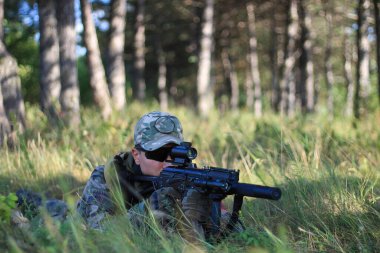 Ormanın gölgesinden ateş eden keskin nişancı rolündeki askeri üniformalı hava yumuşağı asker.
