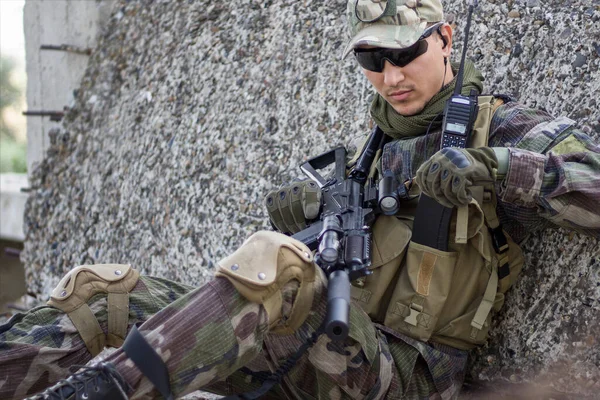 軍用服のAirsoft兵士は コンクリートスラブの後ろにいる間に彼のポケットから弾薬のクリップを取り出します — ストック写真