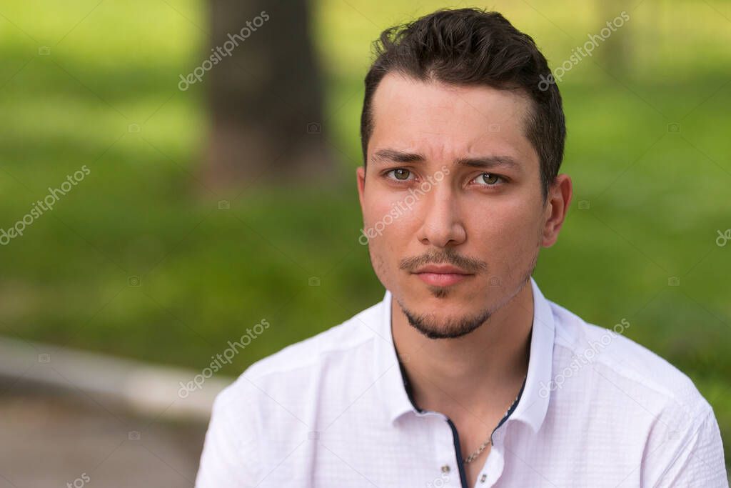 Sad and desperate man in a white shirt on a blurred background. Close-up portrait.