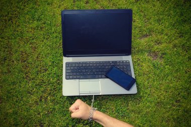 Eli metal bir zincirle dizüstü bilgisayara bağlanmış. Cihazlara, sosyal ağlara ve internete bağımlılık kavramı, bağlılık ve şefkat, uzak çalışma özgürlüğü tuzağı.