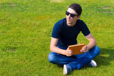 Genç bir adam boş zamanını bir kitapla çimenlikte oturarak geçirir. Ton halinde. Bilginin ve doğayla birliğin faydaları kavramı.