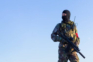 Hava yumuşacık askerler eldivenlerle, kamuflaj üniformasıyla, kar maskesi içinde ellerinde bir silahla mavi gökyüzüne karşı çalışmaya hazırlanıyorlar. Kopyalama arkaplanı