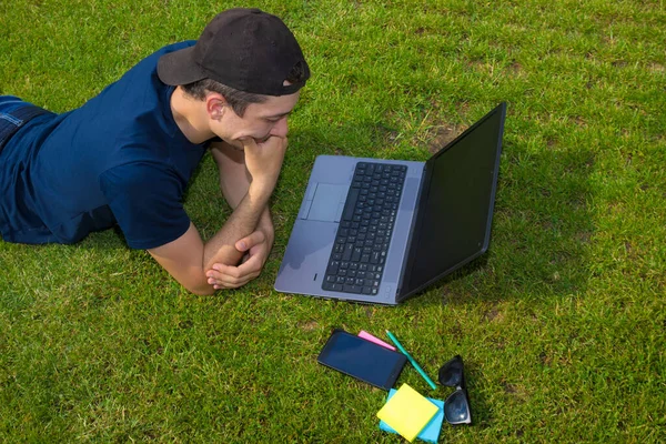 Freelancer works lying on a green lawn with a laptop