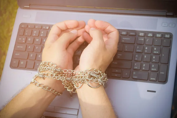 Hands in chains and laptop. The concept of addiction to gadgets and the Internet. The problem of attachment to social networks. Toned. Place for inscription or text.