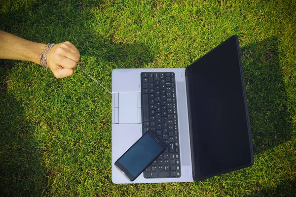 Hand tied to a laptop with a metal chain, toned. The concept of dependence on gadgets, social networks and the Internet, commitment and affection, the trap of freedom of remote work.