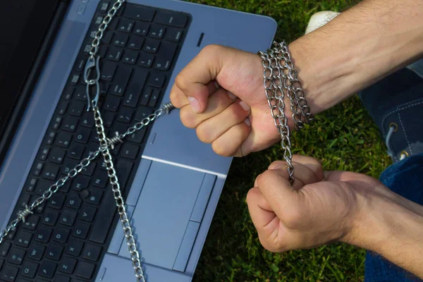 Hands in chains and laptop. The concept of addiction to gadgets and the Internet. The problem of attachment to social networks. Toned. Place for inscription or text.
