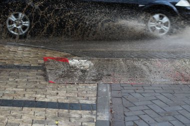 Kaldırımda hızla su birikintilerinden çamur sıçratıyor.