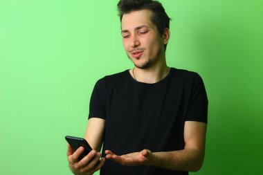 Genç hoşnutsuz adam, yeşil bir arka planda hoşnutsuzluk duygularını ifade eder.