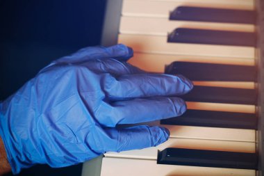 Bir müzisyen, bir ses stüdyosundaki müzik aletinde eldivenle çalar. Covid-19 salgınının gerçeklerinde bir piyanistin hayatı.