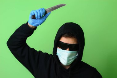 Tıbbi maske takmış genç bir gangster ya da suçlu siyah kapüşonlu güneş gözlüğü takmış elinde bir bıçak tutuyor.