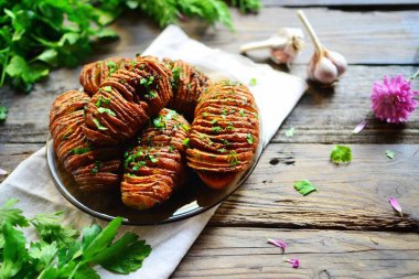 Patates akordeonu. Ahşap zemin üzerinde zeytinyağı, sarımsak ve bitkilerle birlikte fırında patates. Hasselback patatesleri
