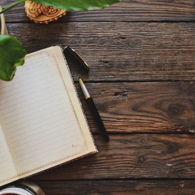 Defter ve kahve, saksı, defter ve kalem, tahta arka plan, üst manzara. Evde çalış. Ofis aksesuarları ve ofis ahşap masası..