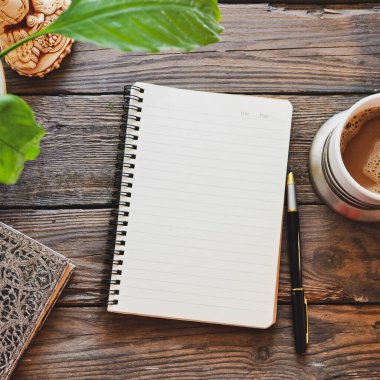 Defter ve kahve, saksı, defter ve kalem, tahta arka plan, üst manzara. Evde çalış. Ofis aksesuarları ve ofis ahşap masası..