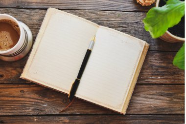 Defter ve kahve, saksı, defter ve kalem, tahta arka plan, üst manzara. Evde çalış. Ofis aksesuarları ve ofis ahşap masası..