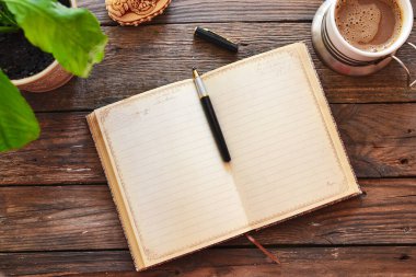 Defter ve kahve, saksı, defter ve kalem, tahta arka plan, üst manzara. Evde çalış. Ofis aksesuarları ve ofis ahşap masası..