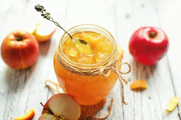 Apple jam in a transparent glass jar. Jam from apples and orange on a light background. Delicious marmalade.