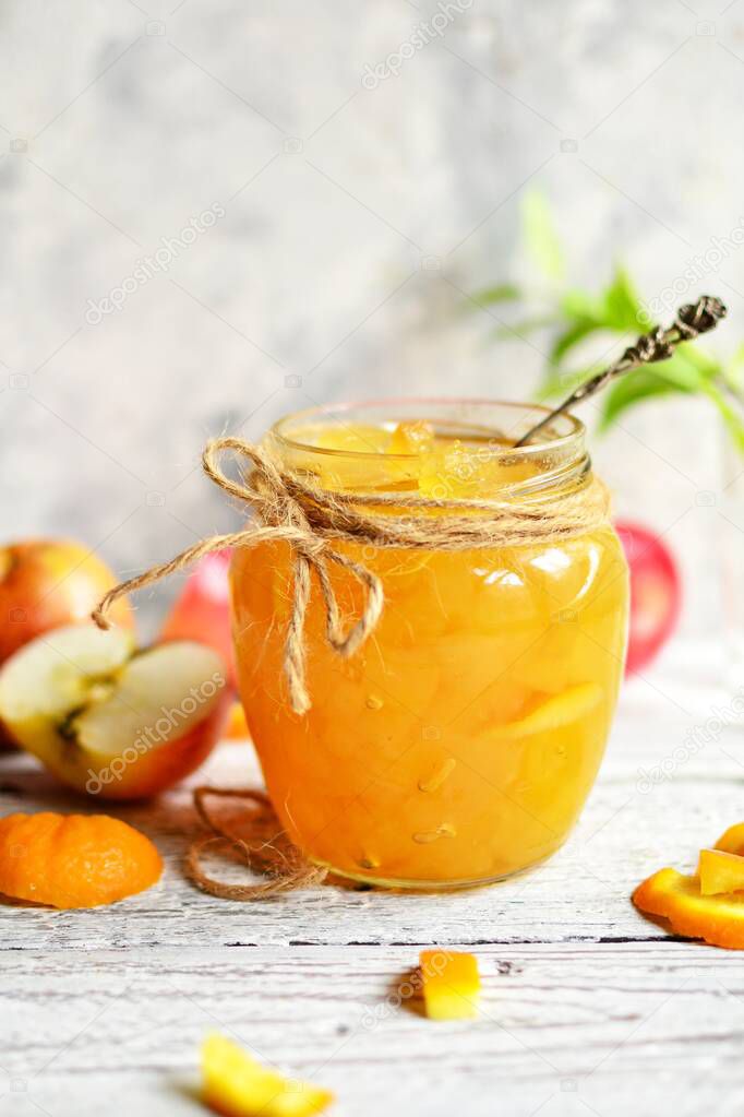 Apple jam in a transparent glass jar. Jam from apples and orange on a light background. Delicious marmalade.