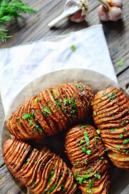Hasselback patatesleri. Fırında pişirilmiş iştah açıcı patates akordeonu. Tahta arka planda patates. Üst görünüm